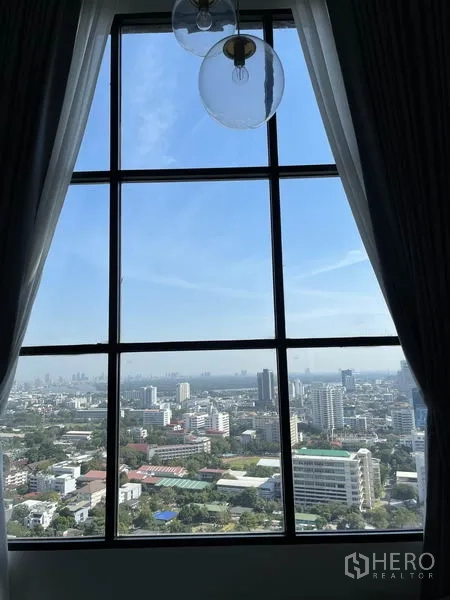 คอนโด ให้เช่าในSathon, Bangkok - วิวสกายไลน์กรุงเทพฯ ผ่านหน้าต่างสูงพร้อมผ้าม่านโปร่งในวันฟ้าใส