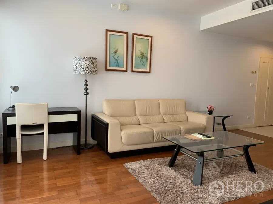 Condominium for rent in Khlong Toei, Bangkok - Contemporary living room featuring a cream leather sofa, study desk, floor lamp and glass coffee table on a rug.