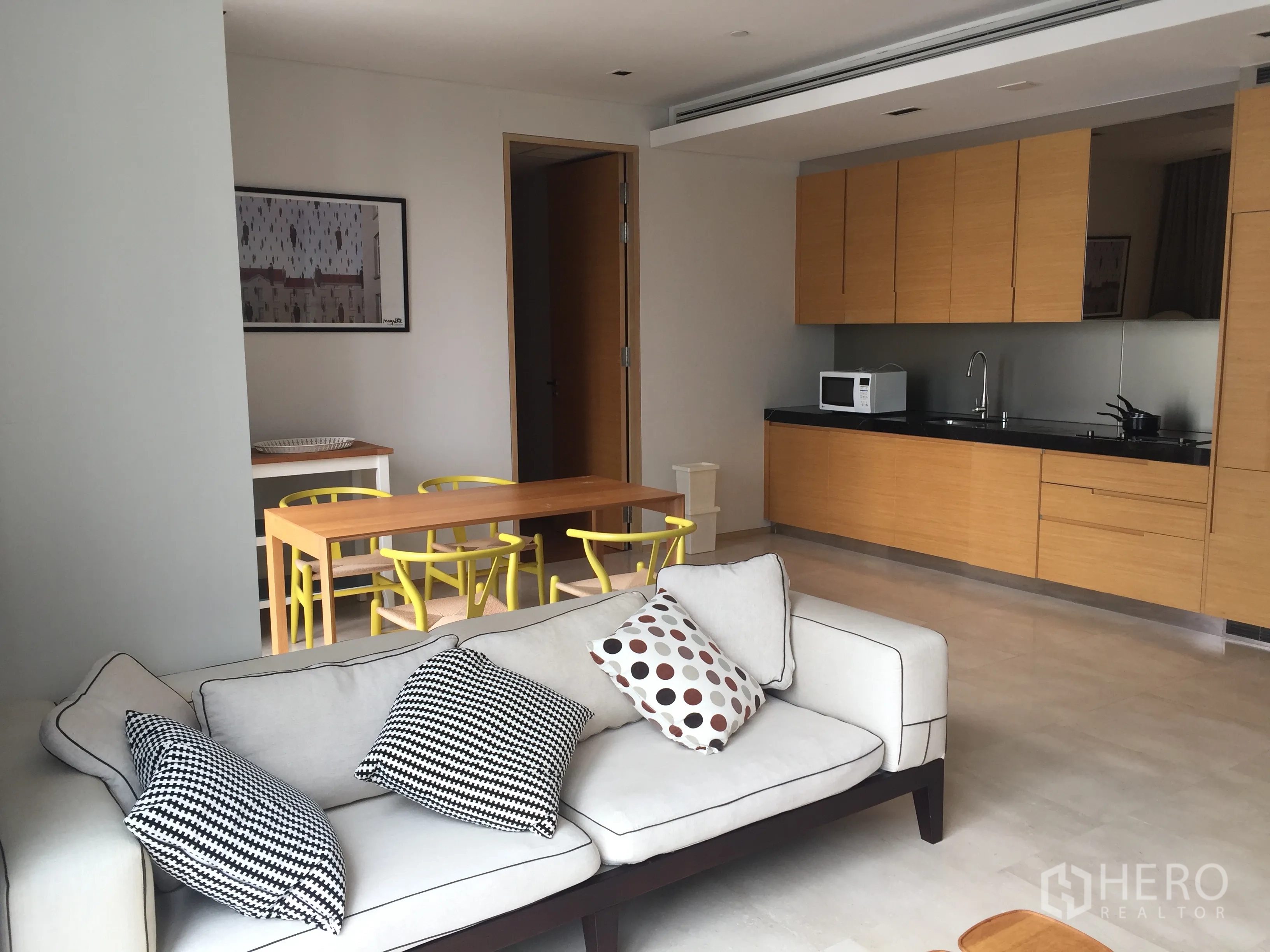Condominium for rent in Bang Rak, Bangkok - Living room with cushioned sofa beside a minimalist wood-finished kitchen and dining set.