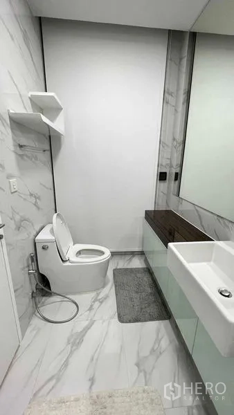 Condominium for rent in Watthana, Bangkok - Second bathroom with toilet, large mirror and under-sink storage on marble flooring.
