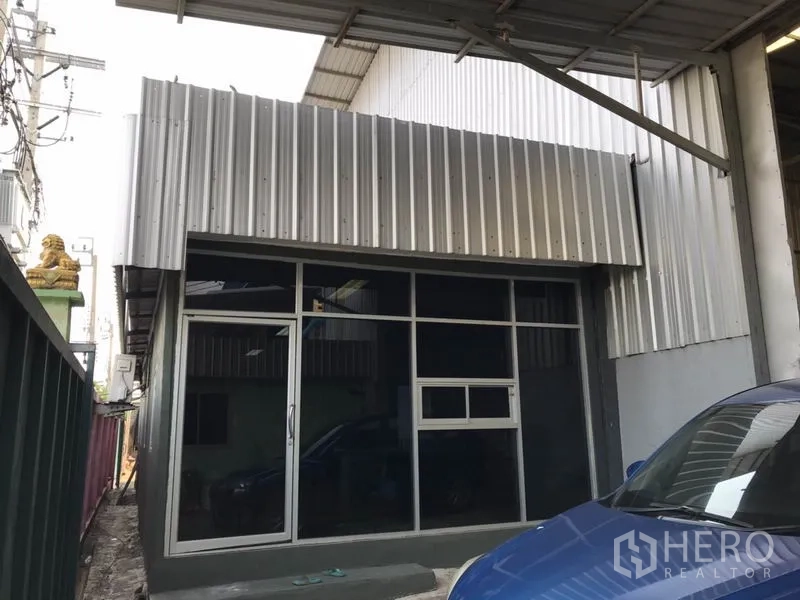 Warehouse for rent in Mueang Samut Prakan, Samut Prakan - Glass-fronted office entry attached to steel warehouse with covered side walkway and parking.