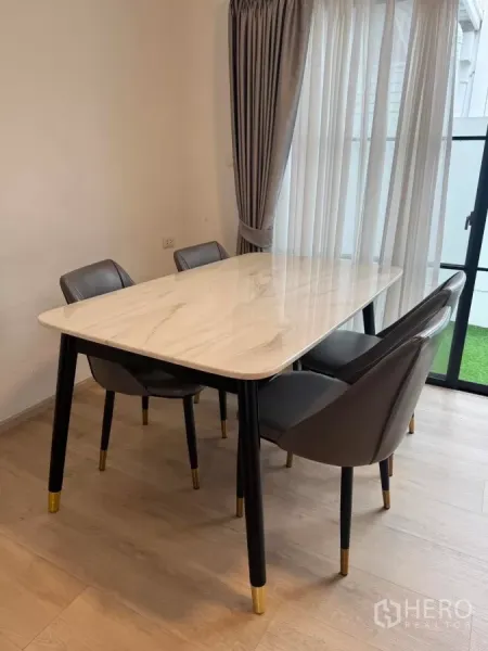 Townhouse for rent in Bang Phli, Samut Prakan - Dining area with marble-top table and four chairs by full-height curtains.