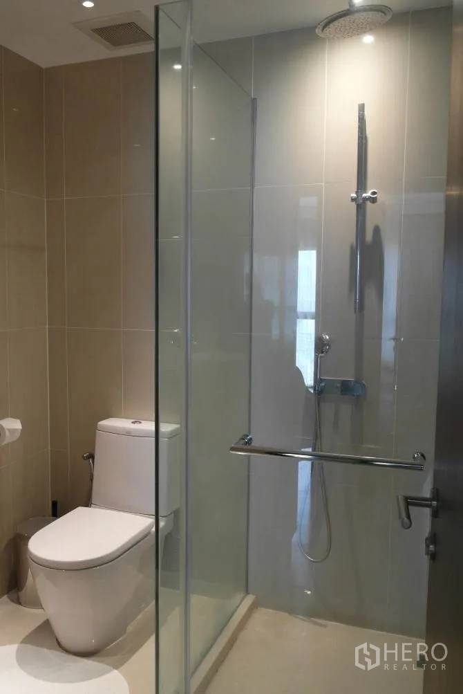 Condominium for rent or sale in Sathon, Bangkok - Bathroom with glass‑enclosed rain shower and toilet in neutral tiles.