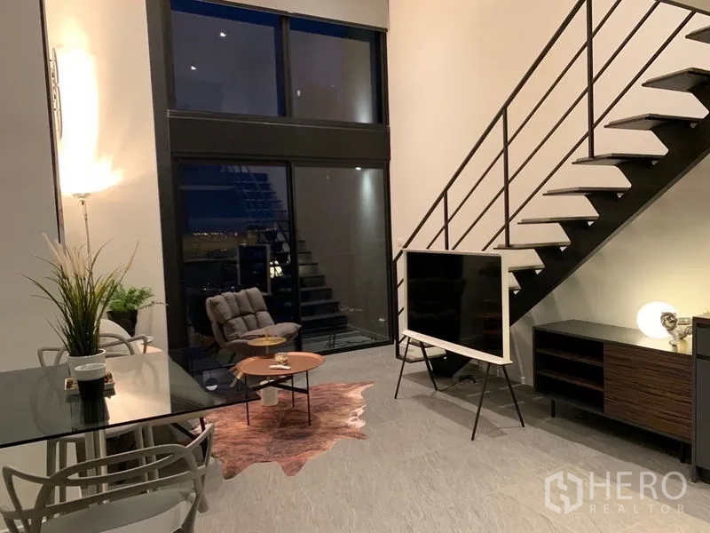 Condominium for rent in Bang Rak, Bangkok - Spacious living area with stairway, TV console and tall windows.