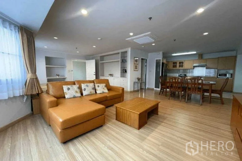 公寓 出租在Watthana, Bangkok - 宽敞客厅，L形皮沙发、餐桌和内置搁架，连接开放式厨房。