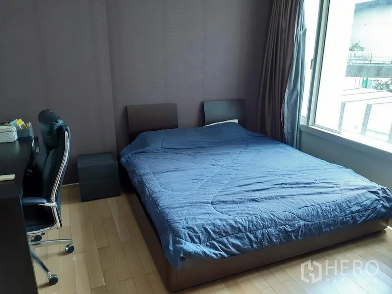 Condominium for rent in Khlong Toei, Bangkok - Cozy bedroom with large window, queen bed, work desk and wood flooring.