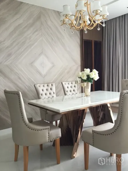 Condominium for rent in Sathon, Bangkok - Marble-top dining table with tufted chairs beneath a gold chandelier and textured feature wall.
