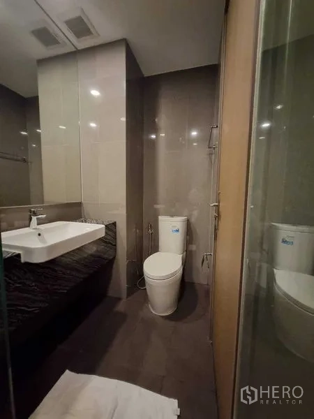 Condominium for rent in Bang Rak, Bangkok - Contemporary bathroom with wall-mounted sink, toilet and glass shower.