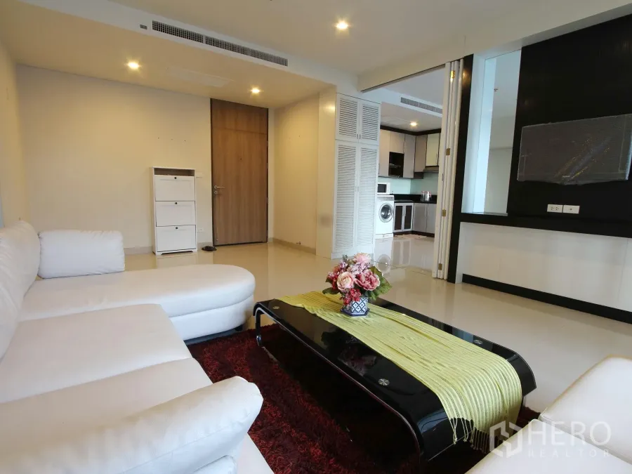 Condominium for rent or sale in Watthana, Bangkok - Spacious Thonglor condo living room in Watthana, Bangkok with white sectional sofa, glossy floors and TV wall opening to the kitchen.