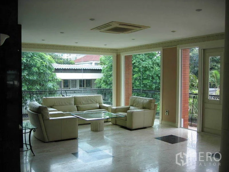 Detached House for rent in Watthana, Bangkok - Bright living room with marble flooring, cream sofas and large windows opening to a balcony and garden views.