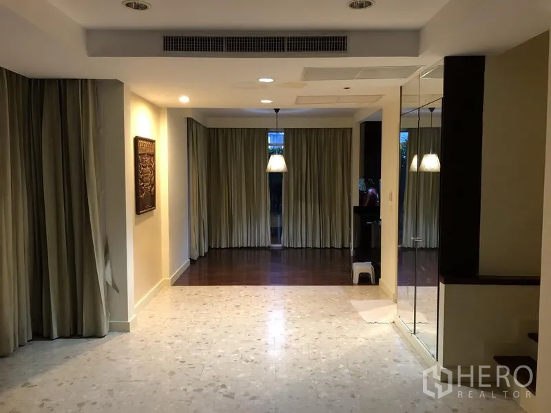 Detached House for rent in Wang Thonglang, Bangkok - Open-plan living and dining area with recessed lights, curtains, and tile-to-wood flooring.
