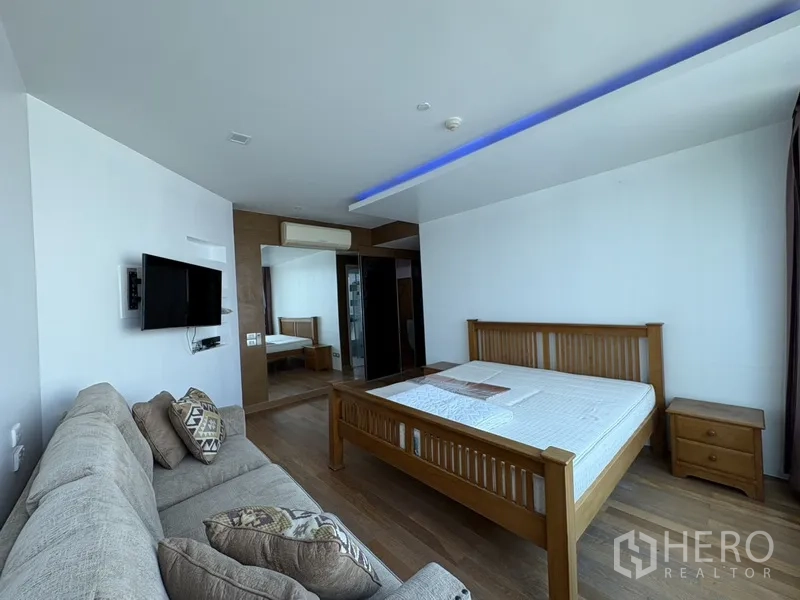 公寓 for rent in Khlong San, Bangkok - 宽敞卧室，木床、沙发、电视与木地板，筒灯照明。