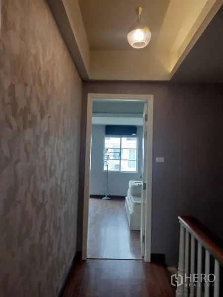 Townhouse for rent in Bueng Kum, Bangkok - Hallway with pendant light leading to a bright bedroom with wood flooring.
