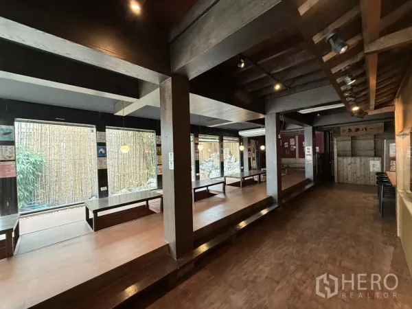 Detached House for rent in Watthana, Bangkok - Open-plan hall with raised wooden seating platforms and floor-to-ceiling windows to the garden.