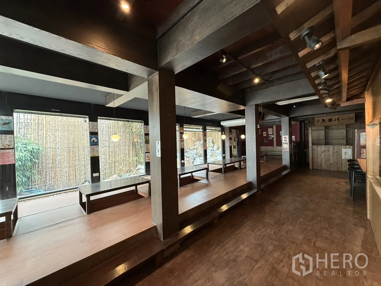 Detached House for rent in Watthana, Bangkok - Open-plan hall with raised wooden seating platforms and floor-to-ceiling windows to the garden.