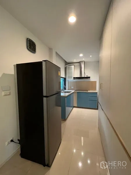 Detached House for rent in Saphan Sung, Bangkok - Galley kitchen with refrigerator, sink and cooktop under ceiling spotlights.