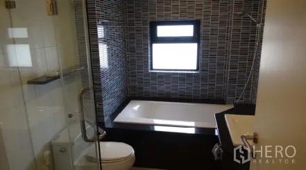 Condominium for rent or sale in Sathon, Bangkok - Bathroom with bathtub beside a window, mosaic wall tiles, and adjacent glass shower.