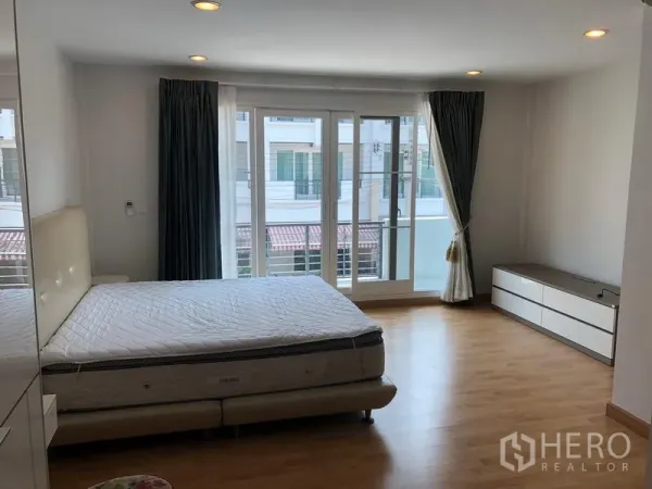 联排别墅 出租或出售在Wang Thonglang, Bangkok - 宽敞卧室，落地窗通向阳台，木地板与低柜储物。
