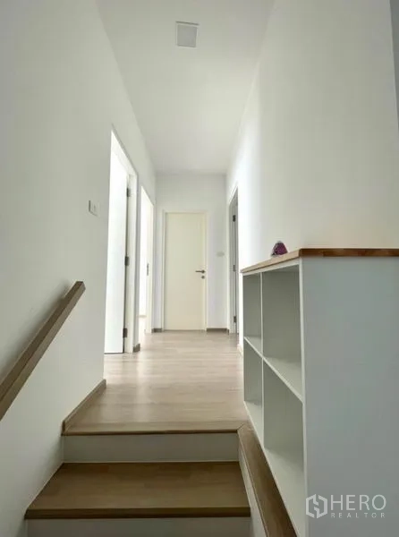 联排别墅 for rent in Prawet, Bangkok - 二层走廊，木质台阶、白色墙面与内置搁架。