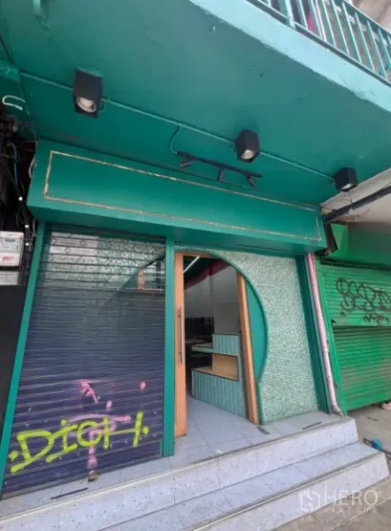 Shophouse for rent in Watthana, Bangkok - Street-level shophouse facade with green signage, curved tiled entry and rolling shutter.