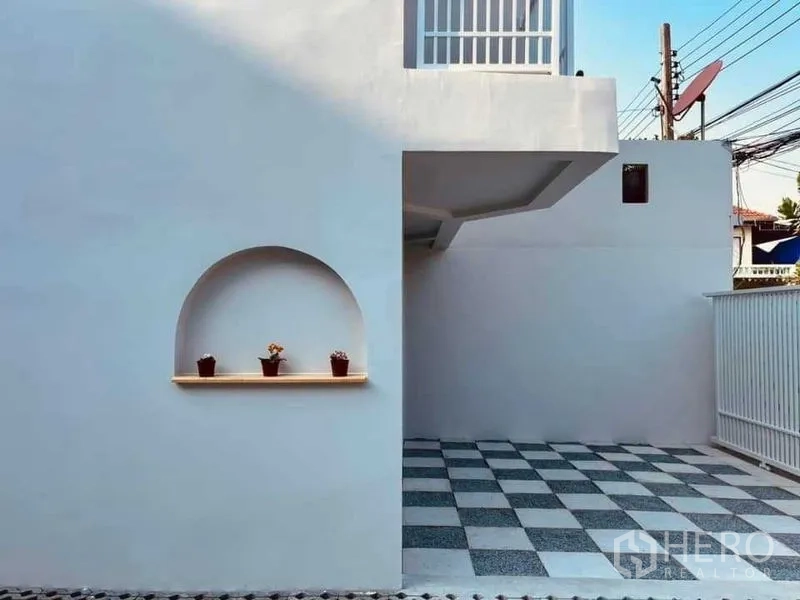 Townhouse for sale in Phra Khanong, Bangkok - Front patio and covered parking with checkerboard tiles and an arched wall niche.