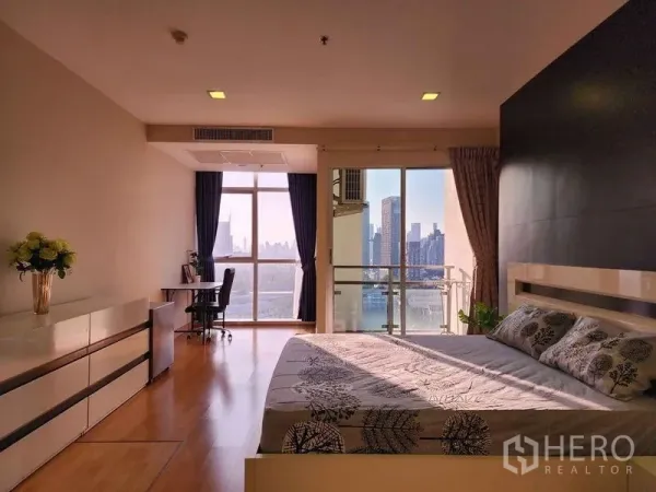 Condominium for rent in Khlong Toei, Bangkok - Spacious bedroom with floor-to-ceiling windows, balcony and city skyline view with a desk area.