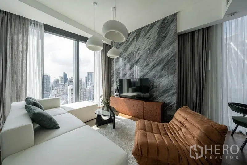 Condominium for rent in Khlong Toei, Bangkok - Bright living room with marble feature wall, white sofa and floor-to-ceiling windows overlooking the Bangkok skyline.