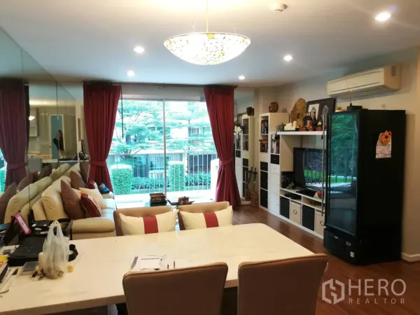 Condominium for rent in Watthana, Bangkok - Open-plan living and dining area with chandelier, mirror wall and sliding doors to the balcony.