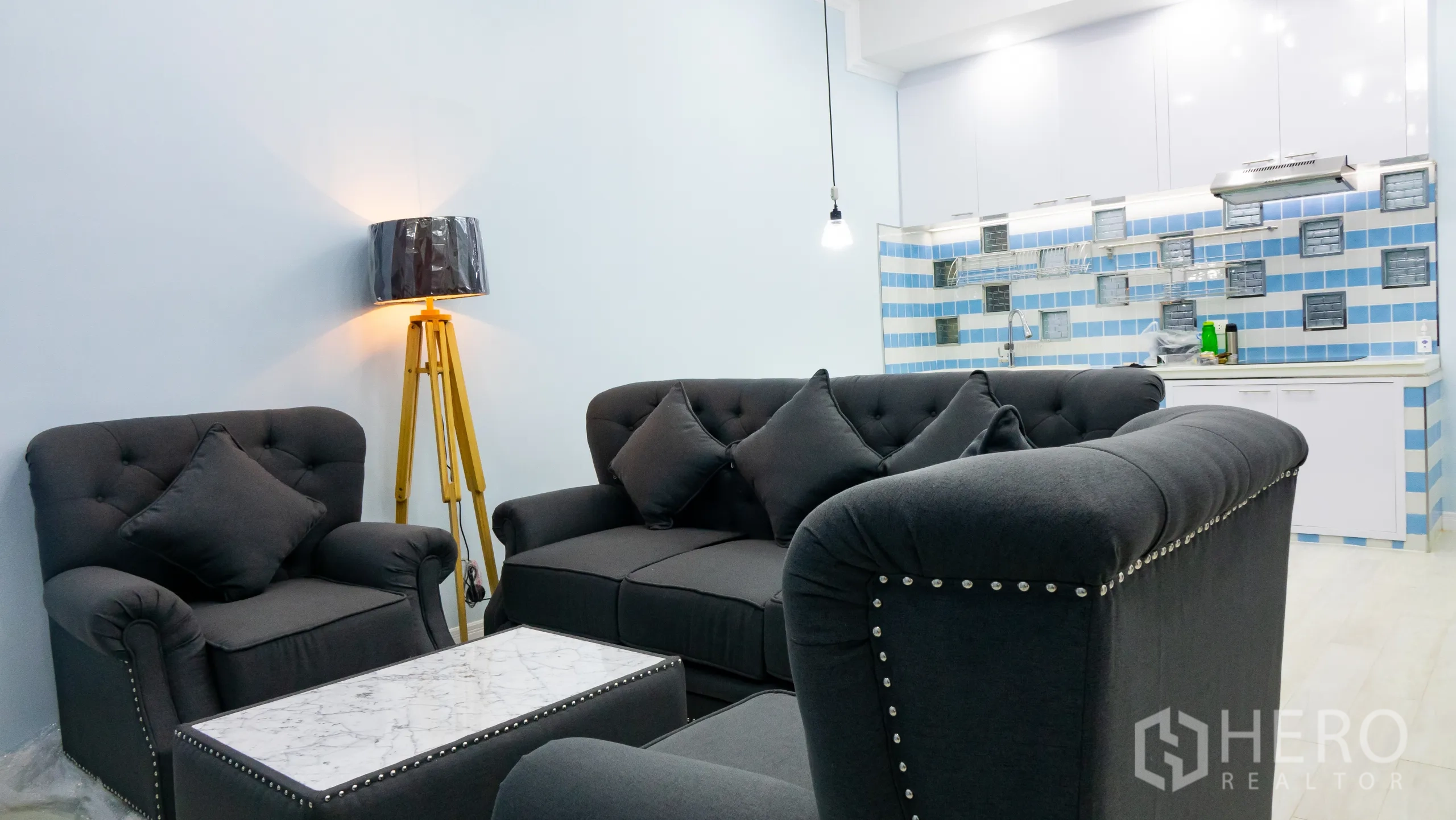 Condominium for rent or sale in Khlong Toei, Bangkok - Open living room with charcoal sofas, marble coffee table and a bright kitchen backdrop.