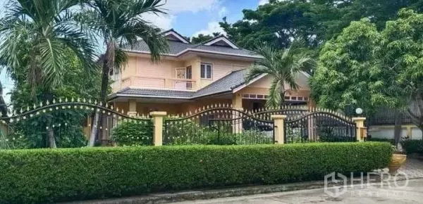 Detached House for sale in Prawet, Bangkok - Street view of house with wrought-iron fence, palm trees and lush greenery.