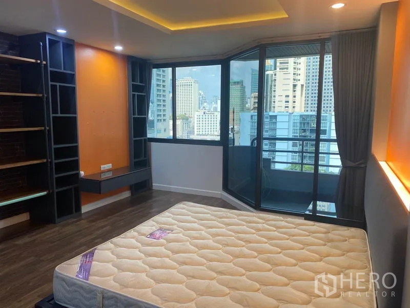 Condominium for rent in Khlong Toei, Bangkok - Master bedroom with corner floor-to-ceiling windows, city skyline view, built-in shelving, and mattress.