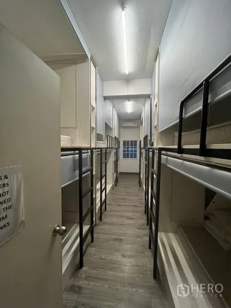 Shophouse for rent or sale in Watthana, Bangkok - Narrow corridor lined with double bunk beds under bright strip lighting.