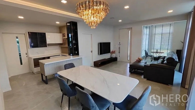 Detached House for rent in Prawet, Bangkok - Open living–dining space featuring a crystal chandelier, TV wall and island kitchen.