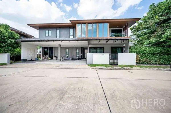 Detached House for sale in Prawet, Bangkok - Front exterior with wide carport, tall windows and gated entrance on a quiet street.
