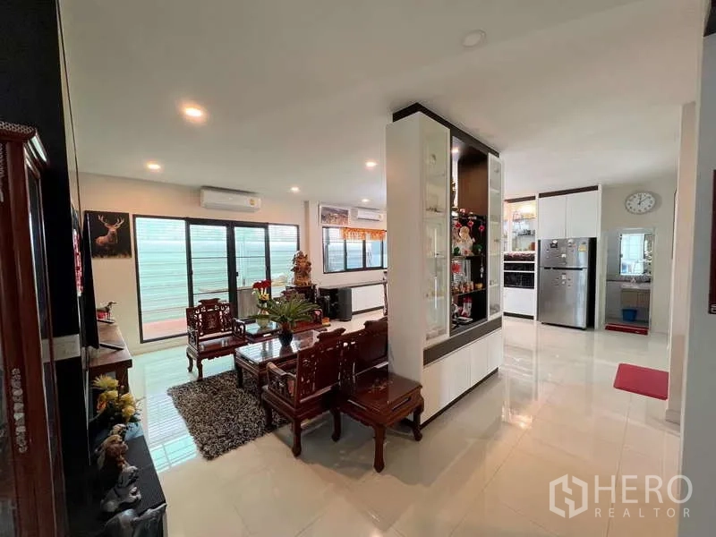 独立式住宅 出售在Prawet, Bangkok - 开放式客厅与餐区，雕花木质家具、玻璃展示柜与推拉窗相连。
