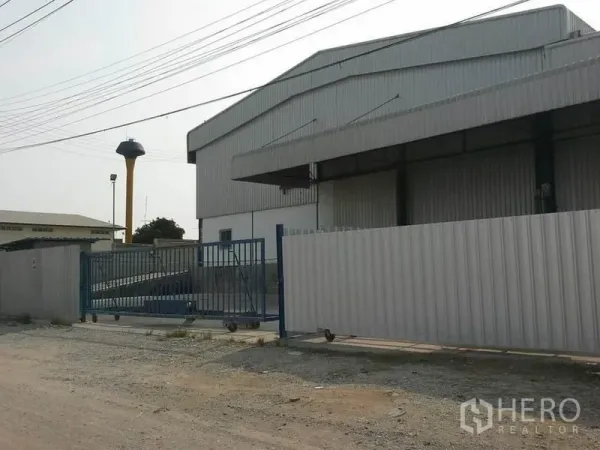 Warehouse for rent in Chon Buri - Warehouse exterior with perimeter fence and sliding gate, wide road access and nearby water tower.