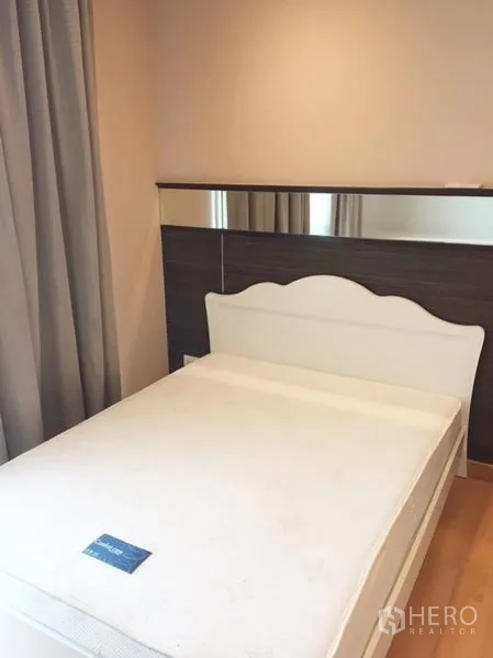 Condominium for rent in Khlong Toei, Bangkok - Cozy bedroom with white bedframe and mirror-accent headboard.
