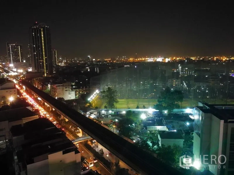 公寓 出租或出售在Watthana, Bangkok - 高楼阳台夜景，可见城市天际线、BTS轨道与点亮的运动场。