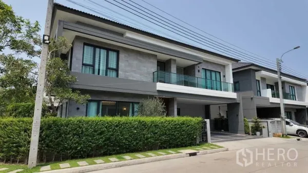 บ้าน ให้เช่าหรือขายในBang Na, Bangkok - ด้านหน้าบ้านเดี่ยวมองจากถนน พร้อมรั้วพุ่มไม้และระเบียงกระจก