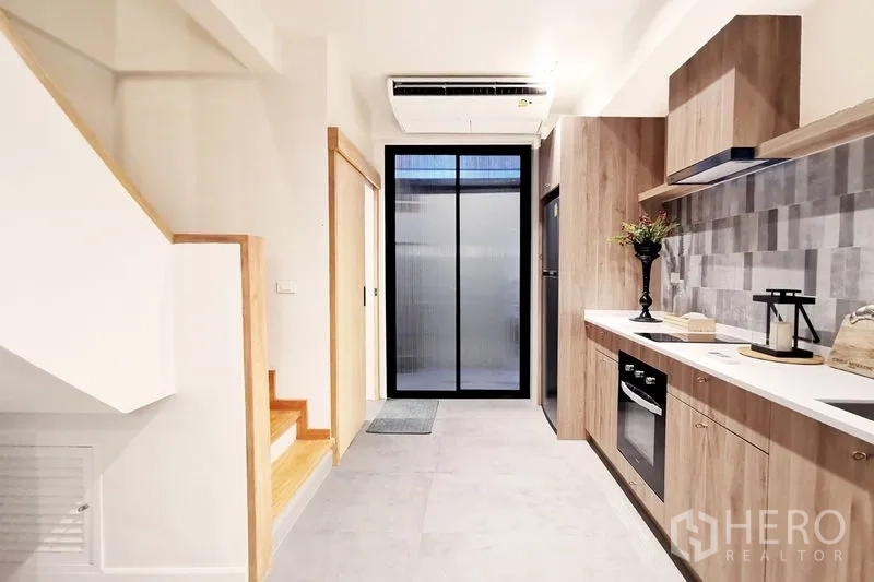 Townhouse for rent in Khlong Toei, Bangkok - Galley kitchen zone with built-in appliances, air-conditioning and glass door to utility area.