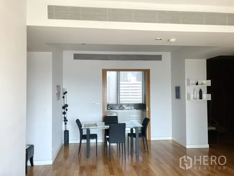 Condominium for rent in Khlong Toei, Bangkok - Dining area with four-seat glass table, wood floors and doorway leading to the kitchen.