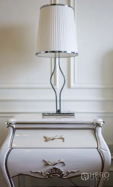 Condominium for rent in Khlong Toei, Bangkok - Close-up of white bedside table with chrome lamp and decorative wall paneling.