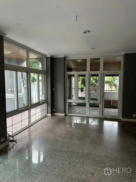 Townhouse for rent in Bang Kapi, Bangkok - Living space with large windows and doors opening to a covered terrace with garden view.