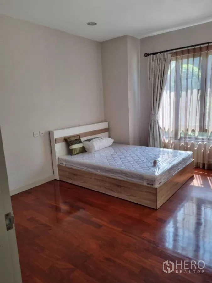 Detached House for rent in Mueang Nonthaburi, Nonthaburi - Sunlit bedroom with polished wooden flooring and a queen bed by a large window.