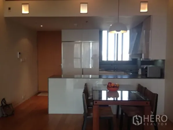Condominium for rent in Sathon, Bangkok - Open-plan kitchen with white cabinetry, island counter, pendant lighting, and a four-seat dining table.