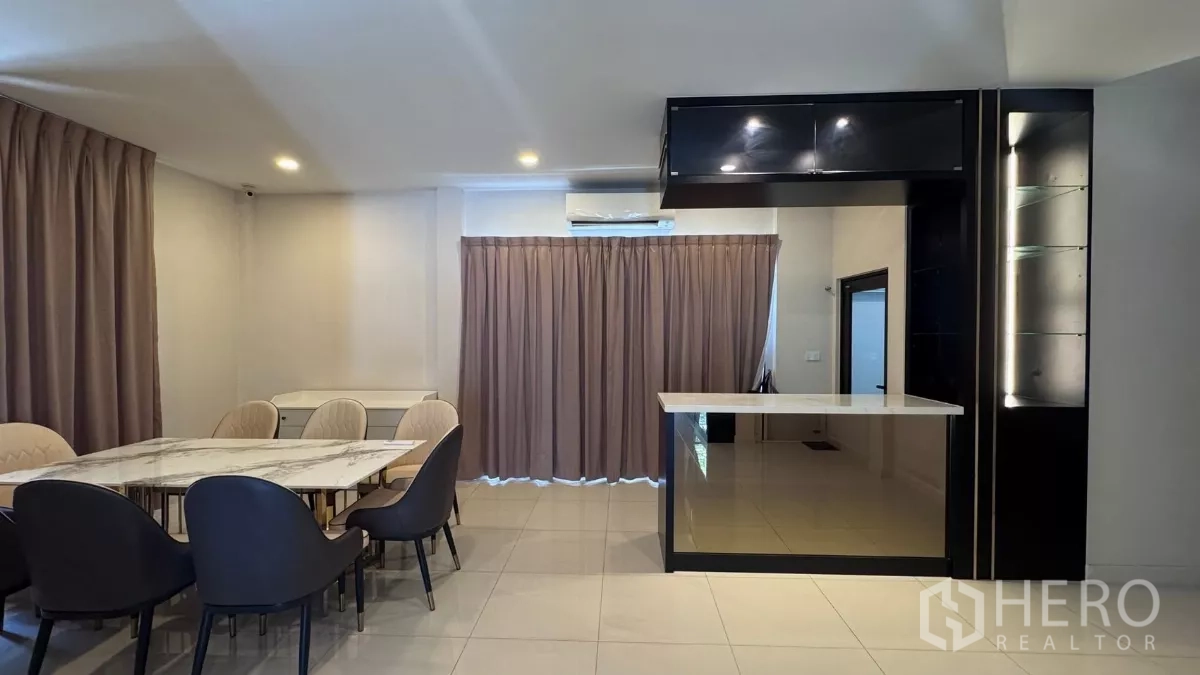 Detached House for rent or sale in Saphan Sung, Bangkok - Dining area with marble‑top table and a bar counter with overhead cabinets, curtained windows providing privacy.