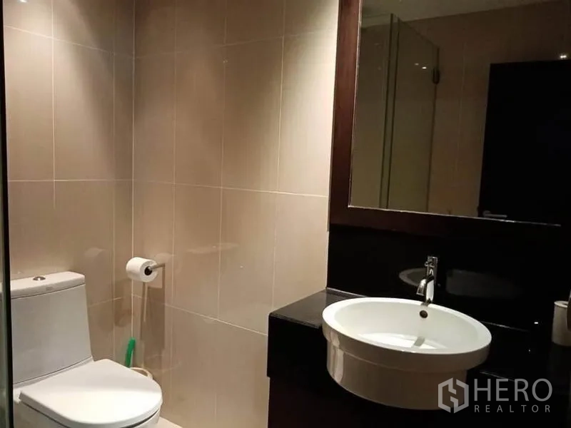 Condominium for rent in Sathon, Bangkok - Bathroom vanity with round basin, large mirror and toilet in a neutral palette.