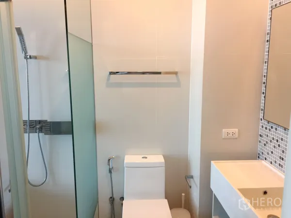 公寓 出租在Watthana, Bangkok - 现代浴室，玻璃淋浴间、白色洗手台与坐便。