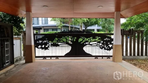 Detached House for rent in Saphan Sung, Bangkok - Covered carport viewed from inside with a sliding gate featuring a tree silhouette design.