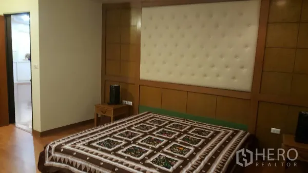 Condominium for rent in Khlong Toei, Bangkok - Cozy bedroom featuring a tufted headboard, warm wood paneling and bedside tables.